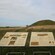 Three placards sit side by side next to the grassy mound of Maeshowe Runes